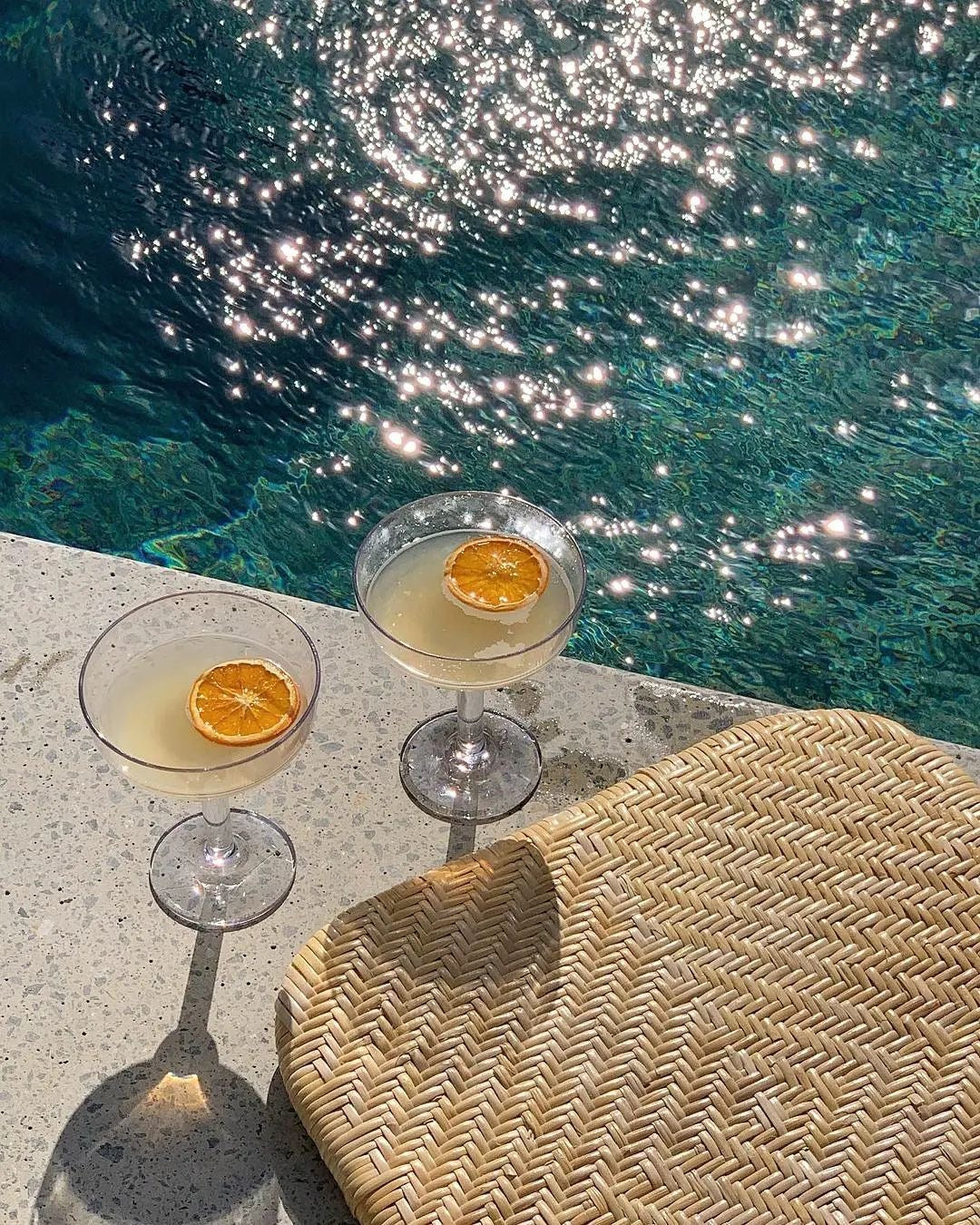 two citrus garnished cocktails by the pool with sparkling crystal clear water