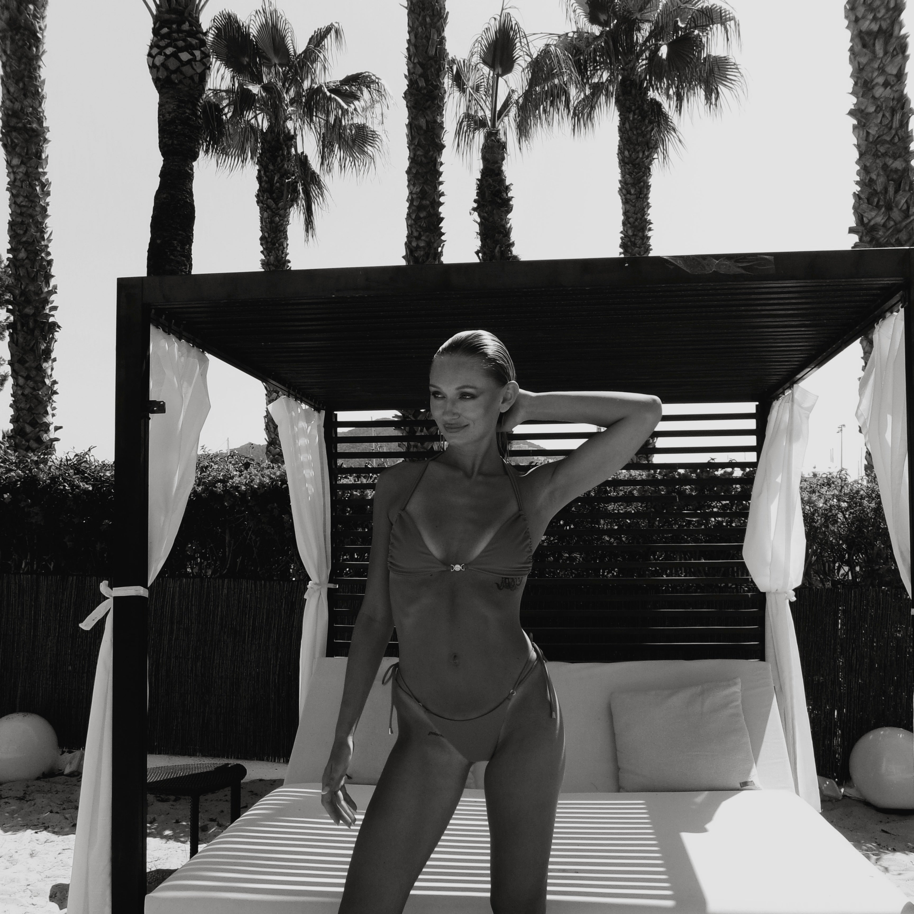 May Rose Chia bikini set Patchouli Brown – model posing at a luxury pool cabana surrounded by palm trees.