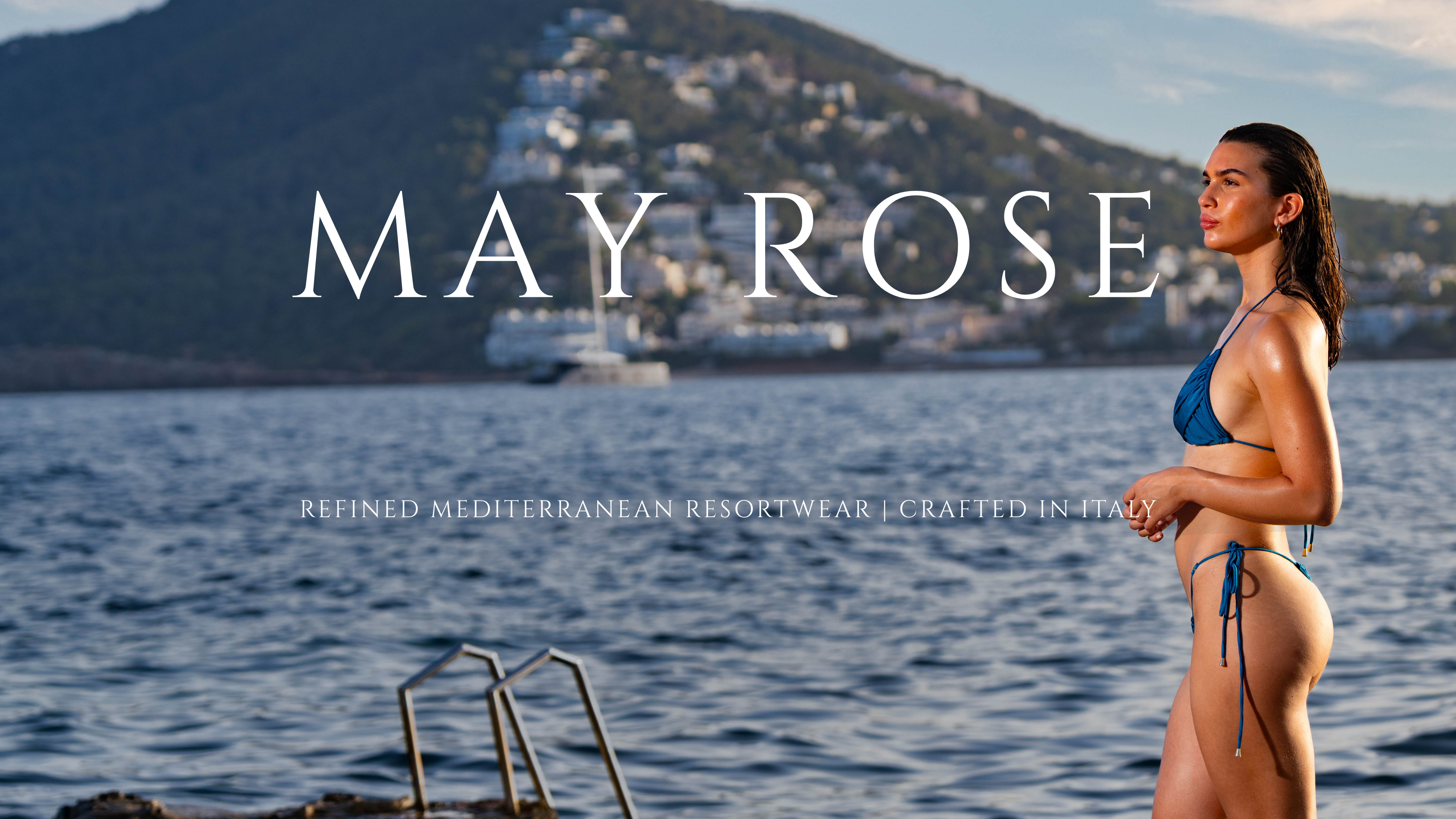 Woman wearing Sofia triangle bikini top and thong bottom in emerald blue by May Rose Swimwear, standing by the sea with Mediterranean coastline in background